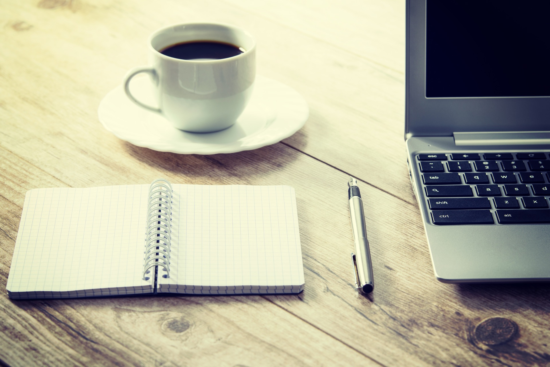 a cup of black coffee on a sourcer next to anote book and a pen and laptop